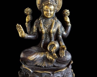 May include: A bronze-colored statue of a seated deity with multiple arms, adorned with intricate jewelry and a halo. The figure holds objects in its hands and is seated on a lotus flower base, set against a black background.