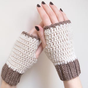 May include: A pair of crocheted fingerless gloves with a brown and white color scheme. The gloves have a brown cuff and a white body with a brown trim.