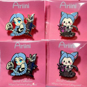 May include: Four enamel pins featuring anime-style characters with blue hair and detailed outfits. One pin shows a character with a bunny, the other with a weapon. The pins are on pink cards with the text "Ariini" and "Secret Collection".
