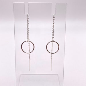 May include: A pair of silver dangle earrings with a small circle pendant and a thin chain hanging from the bottom.