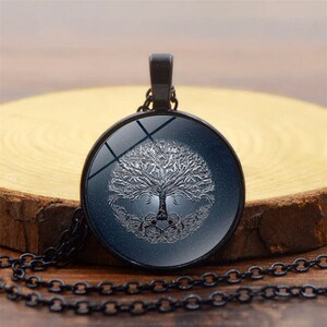 May include: A black chain necklace with a round glass pendant featuring a silver tree of life design on a dark blue background.