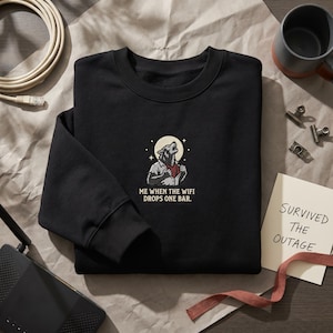 May include: A black crewneck sweatshirt featuring a graphic of a werewolf howling at a moon with the text "ME WHEN THE WIFI DROPS ONE BAR." The design is centred on the chest, showcasing a creature in a shirt with a red undershirt visible.