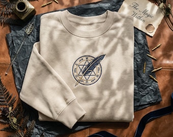 魔女の帽子アトリエ魔法グリフダークアカデミアシャツ、刺繍マンガTシャツ、ストーリーブックファンタジースウェットシャツ、名前入りギフトパーカー、羽根ペンアート