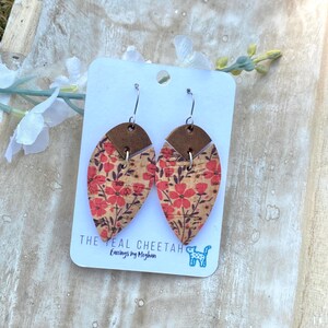 May include: A pair of teardrop-shaped earrings featuring a natural cork texture with a red floral print and dark brown stems. Each earring has a solid brown leather top piece and silver-toned metal hooks. The display card reads THE TEAL CHEETAH.