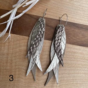 May include: A set of three ceramic mugs with a speckled, matte finish. Each mug features a different color: light blue, cream, and gray. The mugs have a simple, modern design, suitable for coffee or tea.