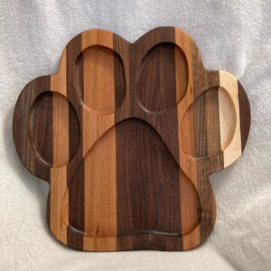 May include: A wooden serving tray shaped like a paw print. The tray is made of different types of wood, including walnut, cherry, and maple. It has five indentations for serving different foods.