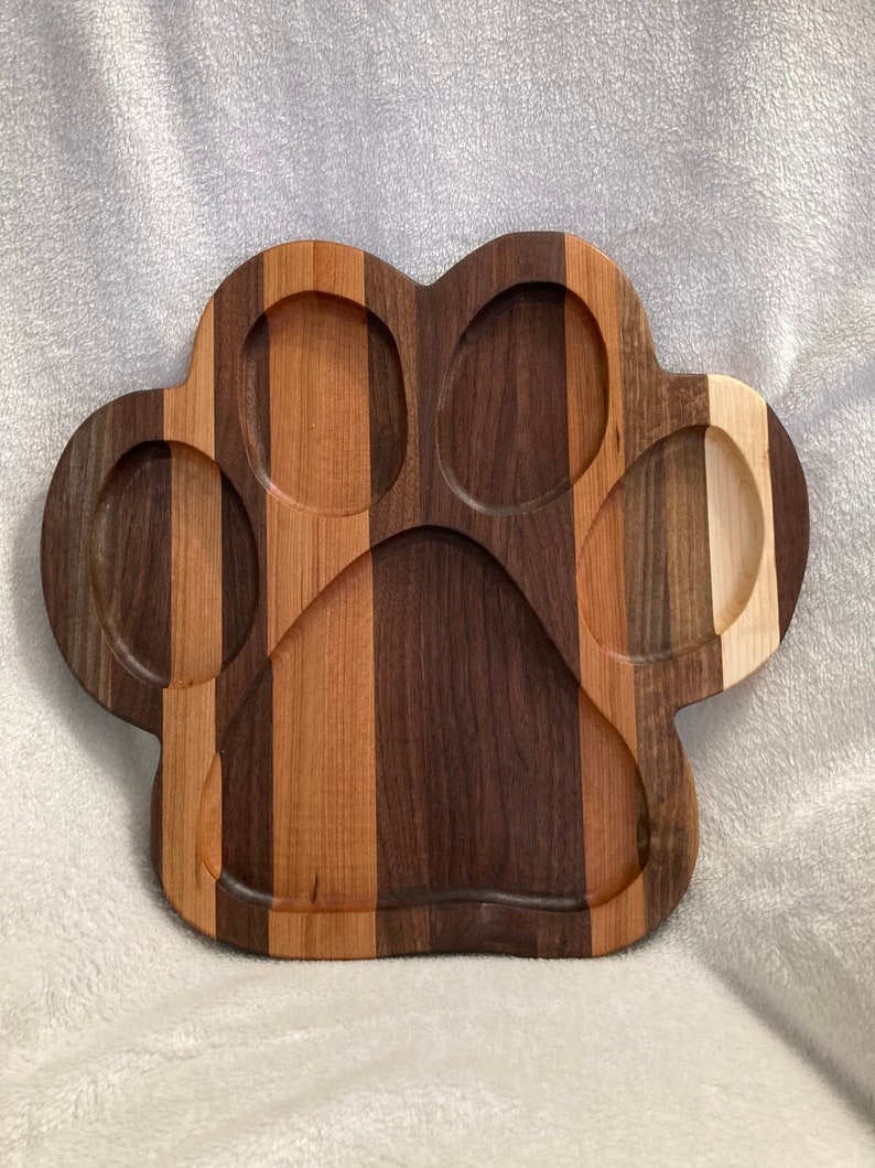 May include: A wooden serving tray shaped like a paw print. The tray is made of different types of wood, including walnut, cherry, and maple. It has five indentations for serving different foods.