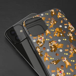 May include: Clear phone case featuring a repeating pattern of cartoon chipmunks, peanuts, and white flowers. The chipmunks are in various poses, with brown and tan fur, red noses, and white teeth. The case is on a black phone.