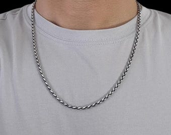May include: A silver chain necklace with a braided design.