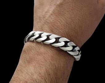 May include: A silver chain bracelet with a curb link design. The bracelet is worn on a person's wrist.
