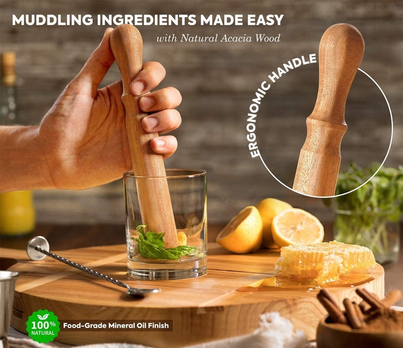 May include: A wooden muddler with an ergonomic handle, made from natural acacia wood. The muddler is being used to crush ingredients in a glass with a clear liquid and green herbs. The muddler has a food-grade mineral oil finish.