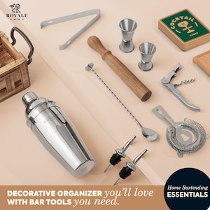 K&ouml;nnte beinhalten: Ein Set Barwerkzeuge in einem dekorativen Organizer. Die Werkzeuge umfassen einen Cocktailshaker, einen Jigger, einen St&ouml;&szlig;el, ein Sieb, Flaschenausgie&szlig;er und einen Barl&ouml;ffel. Der Organizer ist aus Holz und hat eine braune Oberfl&auml;che. Die Werkzeuge sind aus Edelstahl und haben eine silberne Oberfl&auml;che. Das Set ist mit "Home Bartending Essentials" gekennzeichnet.