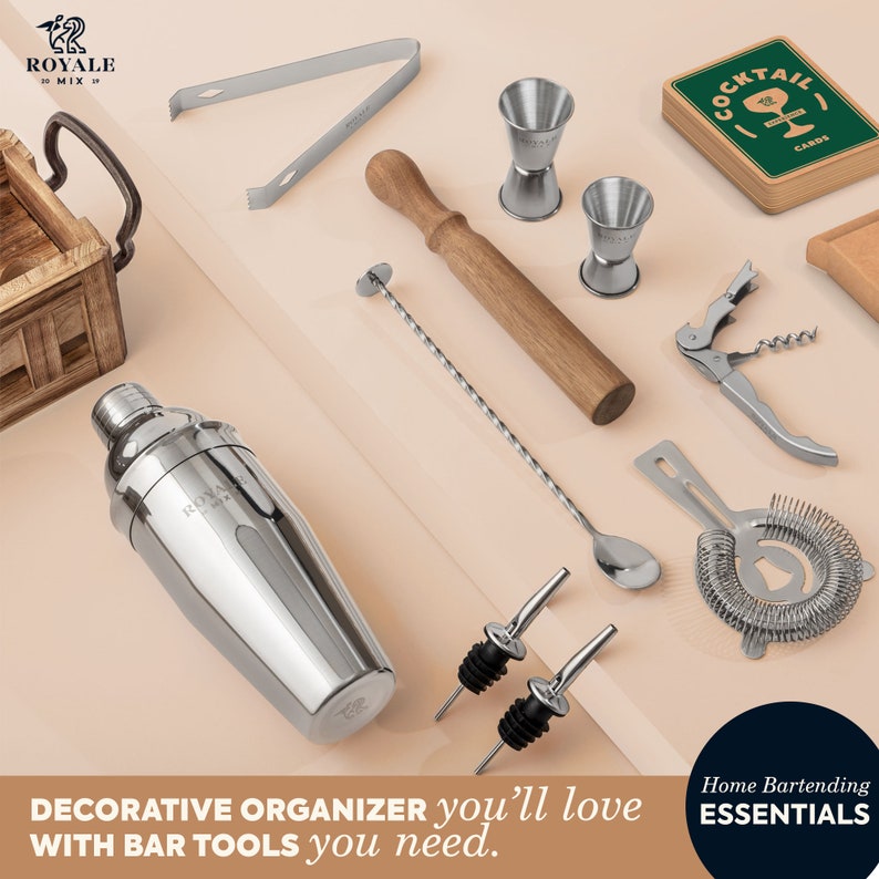 K&ouml;nnte beinhalten: Ein Set Barwerkzeuge in einem dekorativen Organizer. Die Werkzeuge umfassen einen Cocktailshaker, einen Jigger, einen St&ouml;&szlig;el, ein Sieb, Flaschenausgie&szlig;er und einen Barl&ouml;ffel. Der Organizer ist aus Holz und hat eine braune Oberfl&auml;che. Die Werkzeuge sind aus Edelstahl und haben eine silberne Oberfl&auml;che. Das Set ist mit "Home Bartending Essentials" gekennzeichnet.