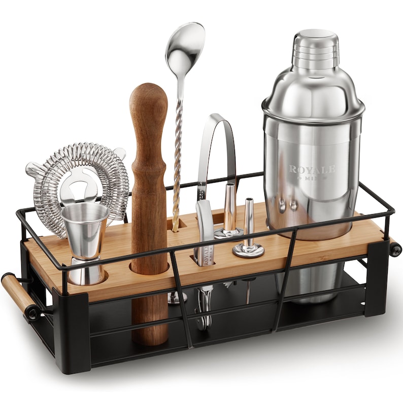 May include: A black metal bar tool holder with a bamboo insert. The holder contains a cocktail shaker, a muddler, a jigger, a strainer, a bar spoon, a bottle opener, and a pair of tongs. The shaker is stainless steel and has the word "ROYALE" engraved on it.