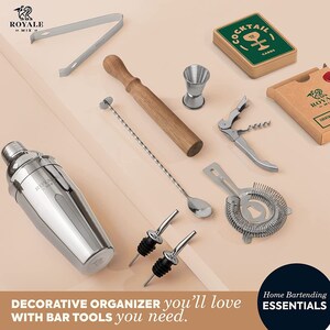 May include: A set of bar tools in a decorative organizer. The tools include a cocktail shaker, a muddler, a jigger, a bar spoon, a strainer, a bottle opener, a corkscrew, a bottle pourer, and a set of cocktail cards. The organizer is made of wood and has a metal frame.