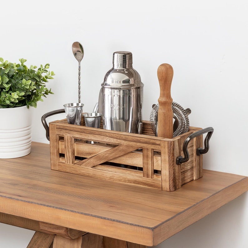 K&ouml;nnte beinhalten: Eine Holzkiste mit Metallgriffen, die einen Cocktailshaker, einen Jigger, einen Barl&ouml;ffel, einen St&ouml;&szlig;el und ein Sieb enth&auml;lt. Die Kiste steht auf einem Holztisch.