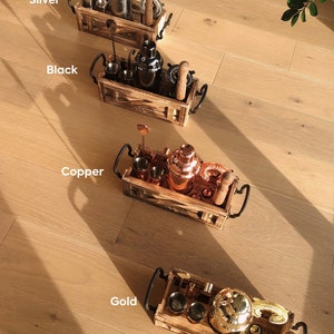 K&ouml;nnte beinhalten: Vier Holzkisten mit Metallgriffen, jede mit einem Cocktailshaker, einem Jigger und anderen Barwerkzeugen. Die Kisten sind mit "Silber", "Schwarz", "Kupfer" und "Gold" beschriftet, um die Farbe der Metallwerkzeuge im Inneren anzuzeigen.