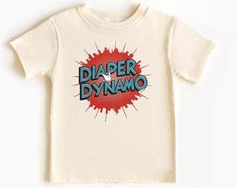 May include: A cream colored short-sleeved t-shirt with a red and blue graphic that says "Diaper Dynamo" with a cartoon baby in a diaper flying in the middle of the graphic.