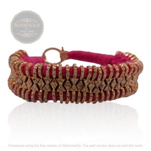 May include: A pink and rose gold bracelet with a diamond-like pattern. The bracelet is made of a thin, flexible material and has a simple clasp.
