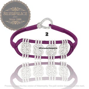 Peut inclure: Un bracelet violet avec des ornements argentés en forme de nœuds. Le bracelet a un fermoir argenté et le chiffre "2". Le logo de la marque "SILVERPALACE Jaipur Since-1986" est en haut à gauche.