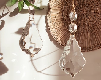 May include: Two crystal teardrop-shaped chandelier prisms hanging from a gold chain. The prisms are faceted and reflect light.