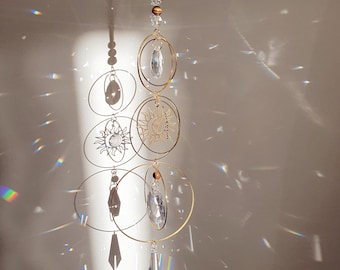 May include: A gold metal suncatcher with three circular frames and crystal prisms hanging from the bottom. The suncatcher is designed to catch light and create rainbows.