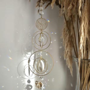 May include: A gold metal hanging mobile with three circular frames and a crystal orb. The mobile features a white shell and a crystal butterfly charm.