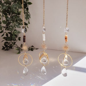 Puede incluir: Tres adornos de atrapasol de oro con gotas de cristal colgando de una cadena. Cada adorno presenta un diseño de estrella y una gota de cristal.