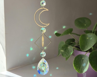 May include: A gold crescent moon-shaped crystal suncatcher with iridescent crystals hanging from it. The suncatcher is hanging from a ceiling and casting rainbows on the wall.