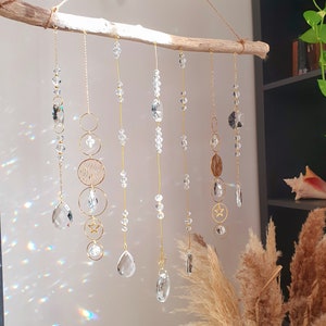May include: A crystal and gold beaded wall hanging with geometric shapes and teardrop crystals. The hanging is attached to a piece of driftwood.