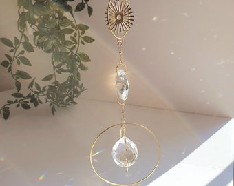 Puede incluir: Un atrapasol de cristal dorado con un prisma de cristal circular que cuelga de un anillo dorado. El atrapasol está suspendido de una cadena con un diseño de estrella.