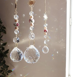 Puede incluir: Tres atrapasoles de cristal con detalles florales y cadenas de eslabones dorados. Cada atrapasol presenta un gran prisma de cristal y cuentas de cristal más pequeñas. Los detalles florales son blancos con patrones florales rosas y rojos.