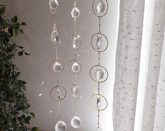 May include: A gold chain with crystal and glass ornaments hanging from the ceiling. The chain has multiple strands with different sized ornaments. The ornaments are clear and reflect light.