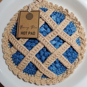May include: Crocheted blue and beige hot pad shaped like a berry pie. The hot pad has a brown tag that says "Berry Pie HOT PAD".