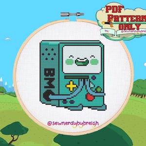 Op de afbeelding: Kruissteekpatroon van een teal BMO-personage uit Adventure Time, in een houten borduurring. Het ontwerp bevat de letters "BMO", een geel plusteken en een rode knop. De tekst "PDF Pattern Only" staat in een wolk.