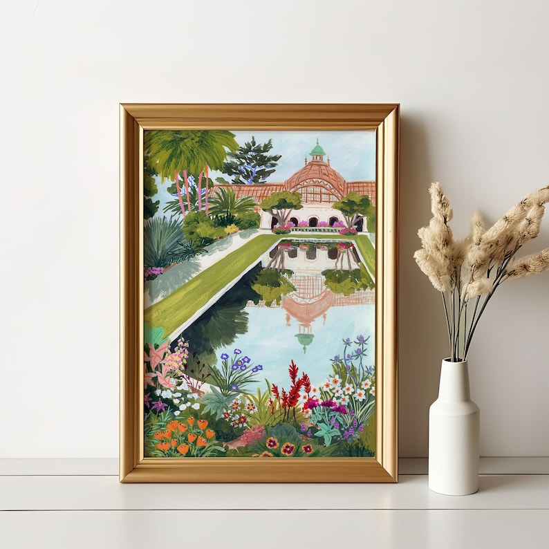 Puede incluir: Una impresi&oacute;n art&iacute;stica enmarcada que presenta una colorida ilustraci&oacute;n de un jard&iacute;n bot&aacute;nico con un estanque reflectante. La obra de arte muestra un edificio con una c&uacute;pula, rodeado de exuberante vegetaci&oacute;n y flores vibrantes. El marco es dorado.