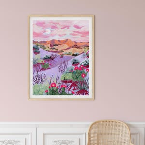 May include: A framed art print shows a desert scene with a pink and purple sky, a full moon, and orange mountains. The foreground features cacti with red flowers and various desert plants in shades of green and purple.