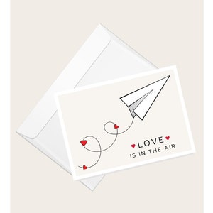 Avion en papier avec coeurs « L'amour est dans l'air » | Saint-Valentin | Anniversaire | Amour et romance | Carte de correspondance vierge élégante