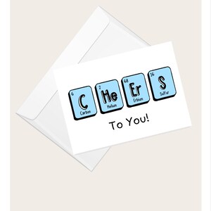 Può includere: Un biglietto di auguri bianco con una busta abbinata. Il biglietto presenta la parola "Cheers" scritta usando elementi della tavola periodica in riquadri blu. La frase "To You!" è scritta sotto.