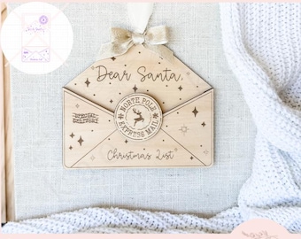 May include: A wooden Christmas ornament in the shape of an envelope, inscribed with "Dear Santa" and "Christmas List". It features a "North Pole Express Mail" emblem and star decorations. Includes a ribbon and bow for hanging. The words "SVG digital cut file laser ready instant download" are at the top.