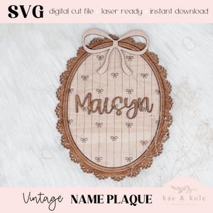 Puede incluir: Placa de nombre vintage de madera con el nombre "Maisyn" en fuente cursiva. La placa ovalada tiene un borde decorativo y detalles de lazo. El texto "SVG digital cut file laser ready instant download" está en la parte superior.