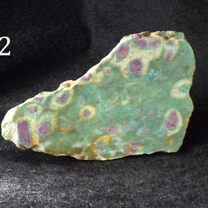 Può includere: Una lastra di pietra naturale con un colore di base verde e crema, con macchie irregolari di rosso intenso. La pietra ha una consistenza ruvida e irregolare e un motivo unico. Il numero "2" è visibile in alto a sinistra.