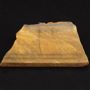 May include: A rough, irregular piece of tiger's eye gemstone with a golden brown colour and a dark brown band across the top.