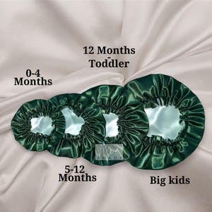 May include: Four green satin bonnets in different sizes for babies and children. The bonnets are labeled with age ranges: 0-4 months, 5-12 months, 12 months toddler, and big kids.