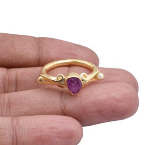 May include: Gold ring featuring a purple gemstone set in a delicate, ornate design.