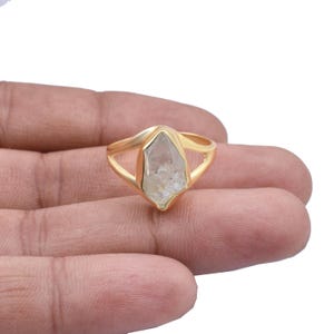 以下が含まれることがあります： 中央に透明な水晶がセットされたゴールドリング。シンプルでエレガントなデザインです。