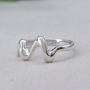 Pode incluir: Um anel de prata com um design ondulado. O anel é feito de metal liso e brilhante e tem um estilo simples e moderno.