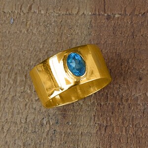 Può includere: Un anello con fascia in oro con una pietra ovale blu incastonata al centro.