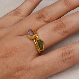 以下が含まれることがあります： 2つのゴールドリングに、原石がセットされています。上のリングはピンクとグリーンの石、下のリングはグリーンの石がセットされています。