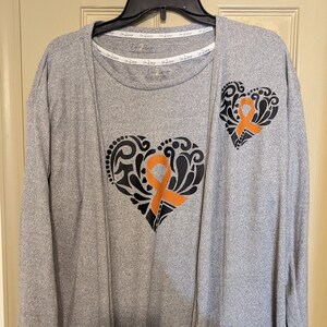 May include: Grey long-sleeved cardigan and a grey t-shirt with an orange ribbon inside a black heart design. The t-shirt has the text "I 2 Love" repeated on the neckline.